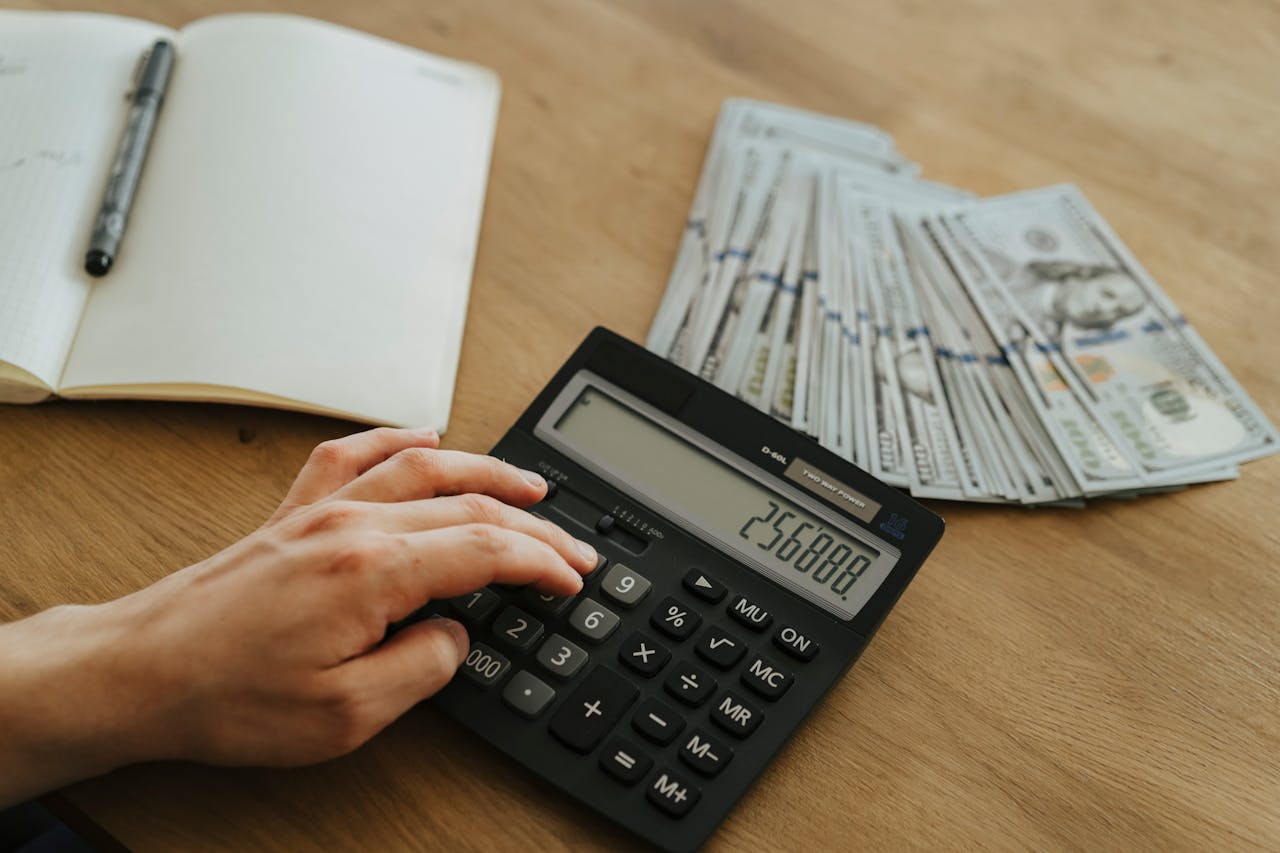 Mastering the First Impression: Your intriguing post title goes here A hand calculates financial figures using a calculator with stacks of cash nearby on a wooden table.